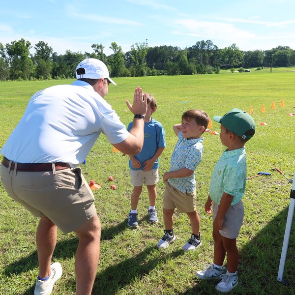 Coach high-fives a line of little golfers